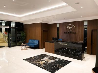 Recepción moderna de hotel con mostrador negro, sofá de cuero y baldosas de mármol claro.