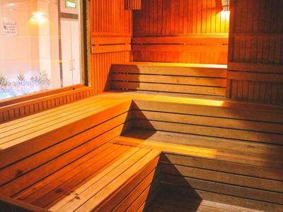 Sauna de madera con bancos a varios niveles y ventana hacia la ducha adyacente.