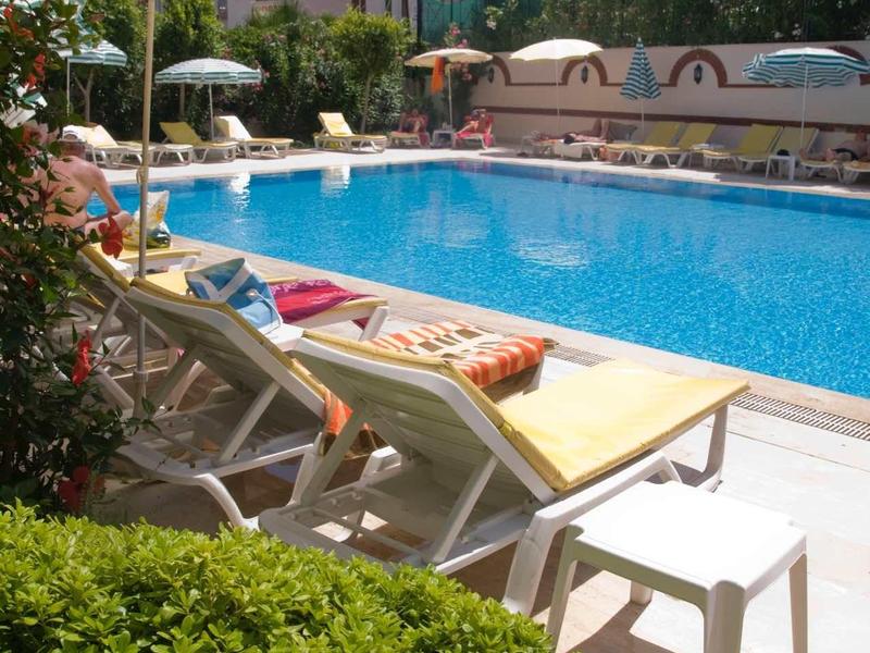 Piscina dell'hotel invitante con sedie a sdraio, ombrelloni e vegetazione circostante sotto un cielo soleggiato.