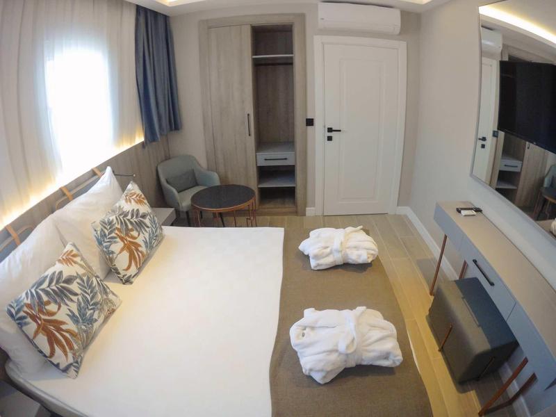 Camera d'hotel luminosa con letto grande, tre cuscini, due accappatoi e TV moderna.