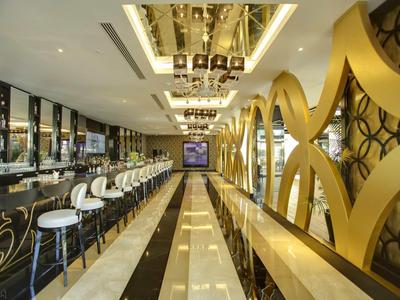 Luxuriöse Bar mit langen weißen Hockern, glänzendem Marmorfußboden und goldenen Wandelementen.