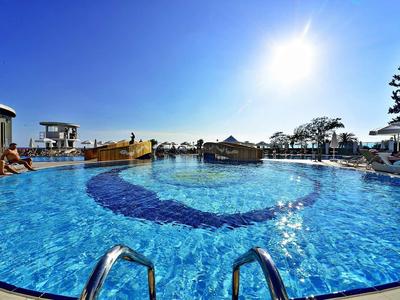 Runder Außenpool mit klar blauem Wasser, Sonnenschein und Liegestühlen bei klarem Himmel.