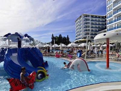 Außenpool mit buntem Wasserspielgerät und angrenzendem Hotel unter blauem Himmel.