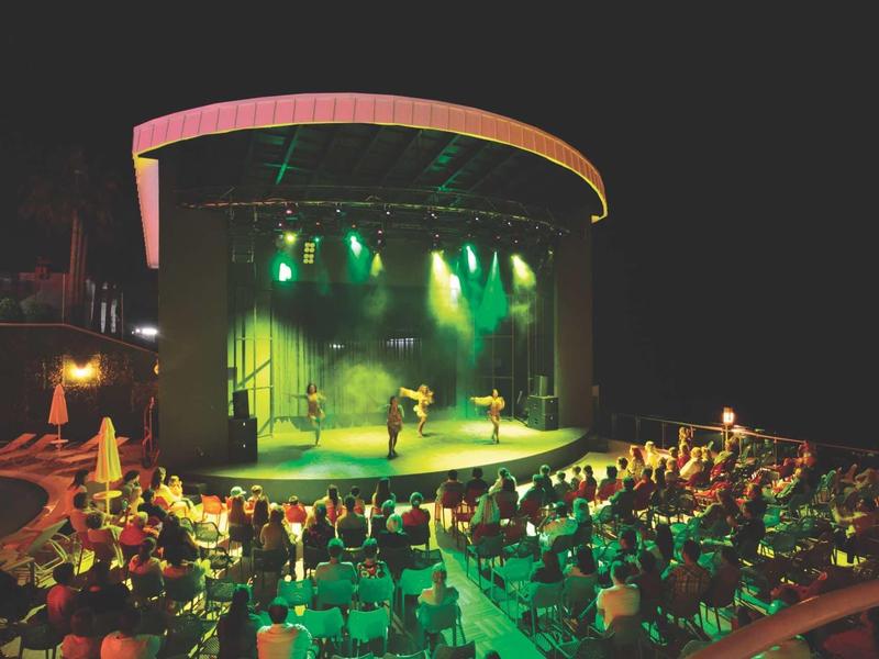 Večerní venkovní představení na osvětleném pódiu před sedícím publikem.