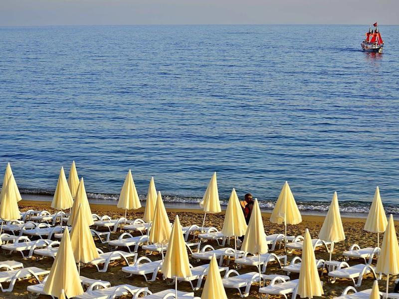 Pláž s žlutými slunečníky a lehátky, klidné moře s červenou bójí v dálce.