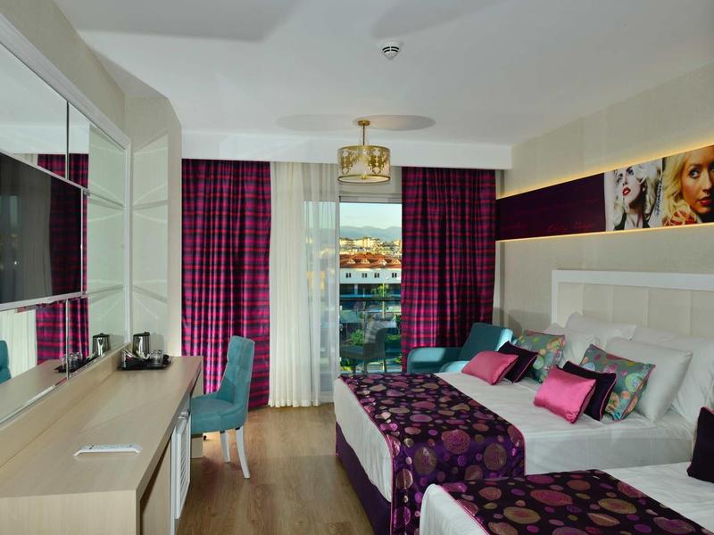 Elegantní hotelový pokoj s manželskou postelí, barevnými polštáři a výhledem na balkon.