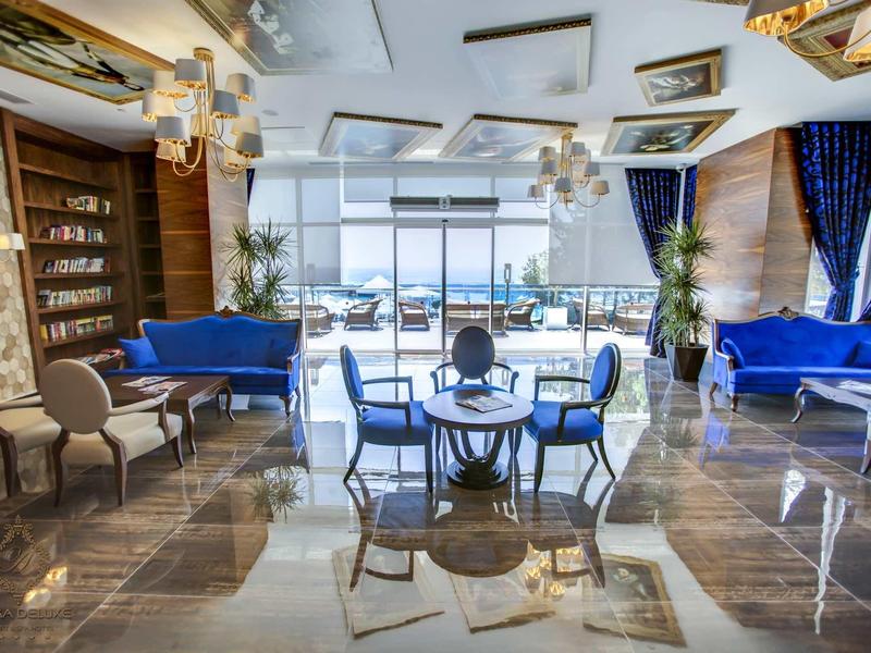 Elegantní salonek s modrými pohovkami a výhledem na oceán přes velká okna.