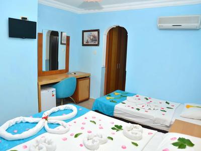 Camera d'hotel azzurro chiaro con due letti singoli, scrivania, sedia, specchio, TV e aria condizionata.