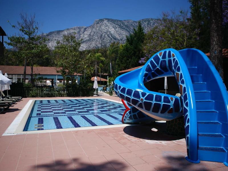 Leisure pool with blue slide and mountains in the background on a sunny day.