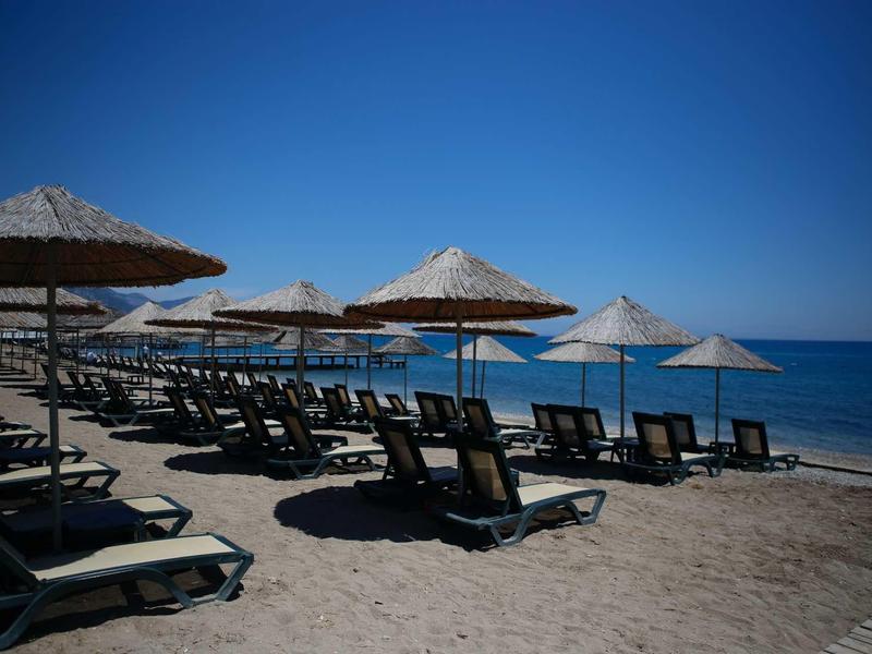 Empty sun loungers and straw umbrellas on the sandy beach with clear blue sea in the background.