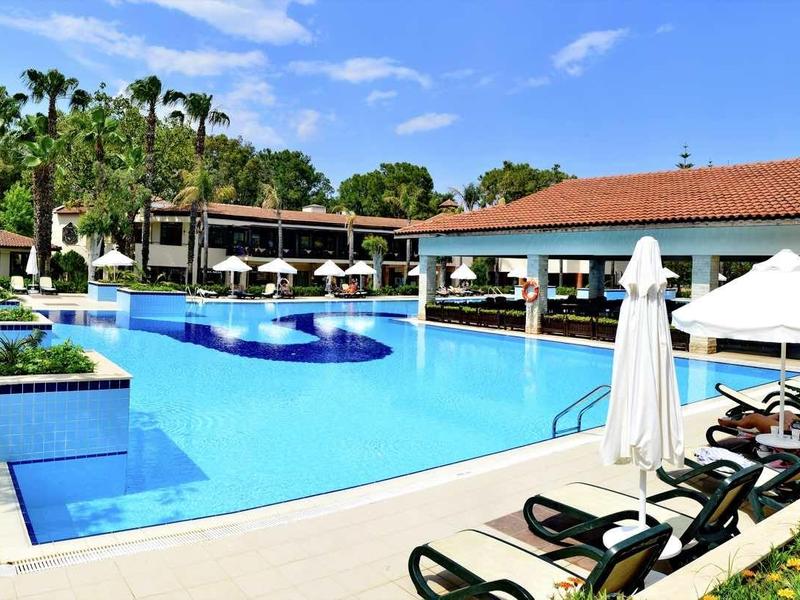 Large hotel pool with lounge chairs, umbrellas, and tropical surroundings on a sunny day