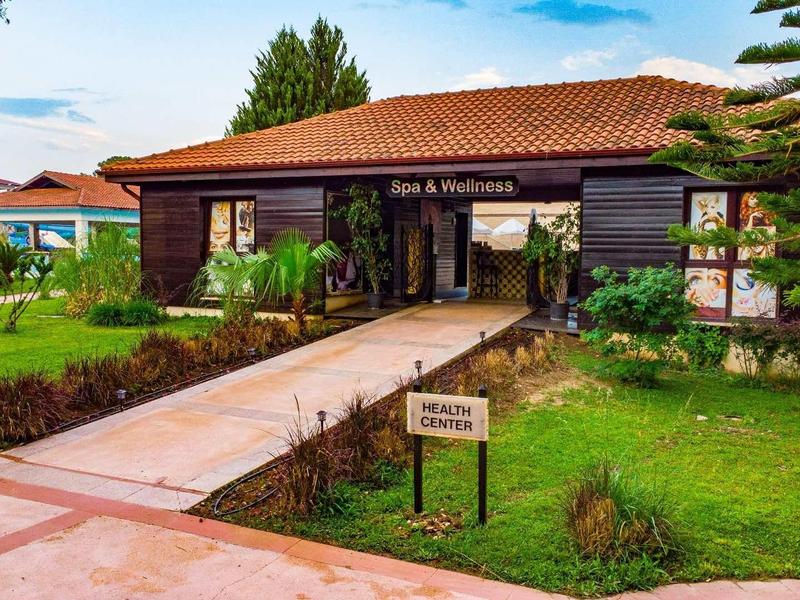 Resort entrance with a low building, green lawn, and path leading to reception.