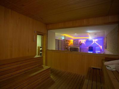 Holzsauna mit Sitzbänken, Kabine mit Fenster zu einem Raum mit buntem Licht und Monitor.