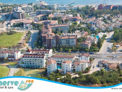 Luftaufnahme eines Küstenorts mit Hotels, Straßen, Bäumen und einem Meer im Hintergrund.