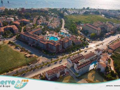 Luftaufnahme eines Resorts mit großen Gebäuden, Pool, Grünflächen und Blick aufs Meer im Hintergrund.