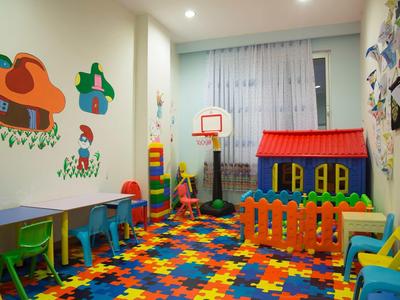 Buntes Kinderzimmer mit Spielmatte, Mini-Basketballkorb, Spielhaus und farbigen Stühlen an der Wand.