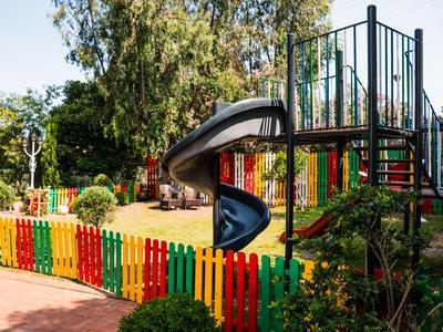 Kleurrijke speeltuin met glijbaan, omgeven door een meerkleurige houten omheining en omringd door bomen.