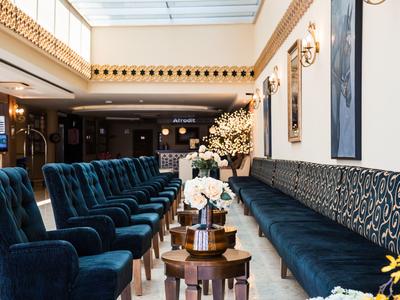 Elegante hotel lobby met fluwelen blauwe stoelen en lange gestoffeerde banken naast tafels met bloemenarrangementen.