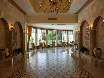 Lichte hotellobby met grote ramen, betegelde vloer en zitgedeeltes met planten.