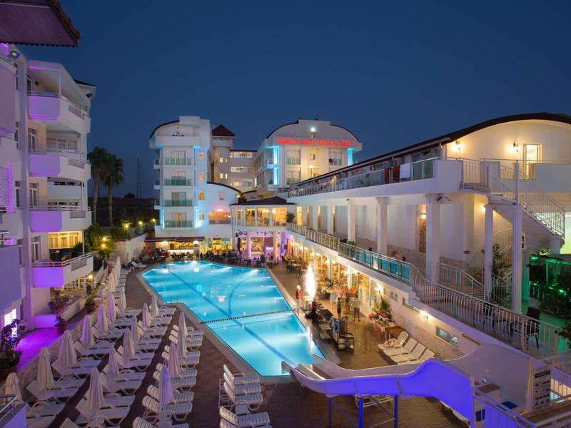 Nocny widok hotelu z oświetlonym basenem i miejscami do siedzenia na tarasie.