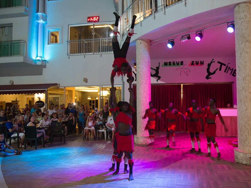 Pokaz akrobatyczny z piramidą ludzką w oświetlonym wnętrzu przed widownią.