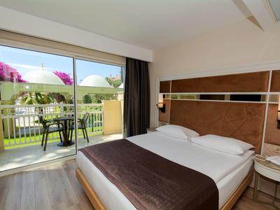 Knus kamer met tweepersoonsbed en terras met tuinmeubilair in daglicht.