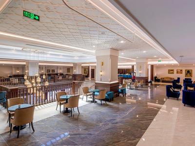 Ruim modern hotel loungegebied met fauteuils en tafels op een lichte marmeren vloer.