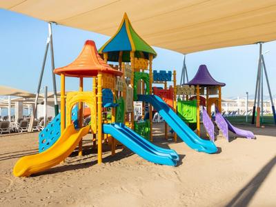 Kleurrijk kinderspeeltoestel met glijbanen onder zonnescherm op zandstrand.