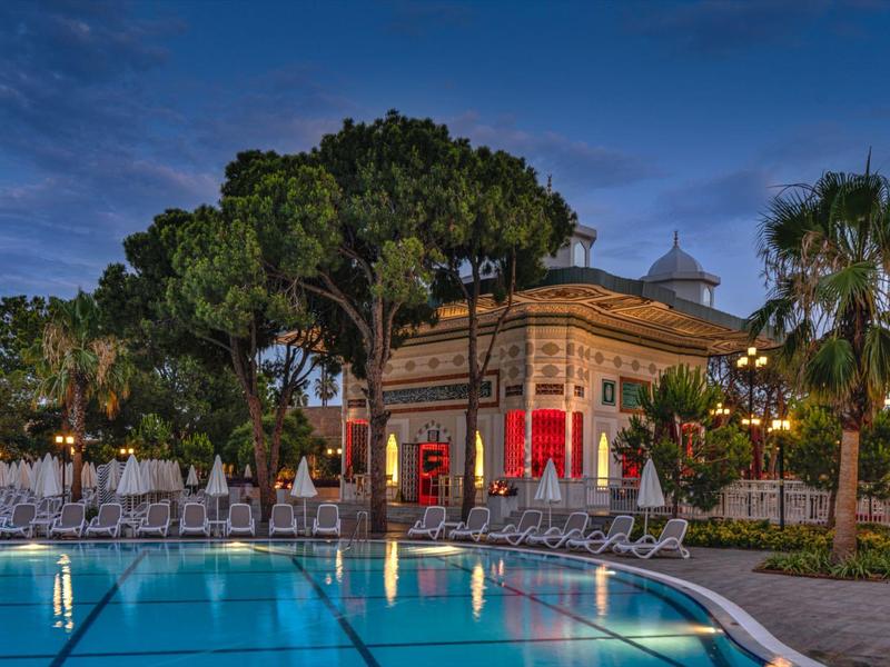 Verlicht zwembad voor een historisch gebouw bij schemering, omringd door palmbomen.