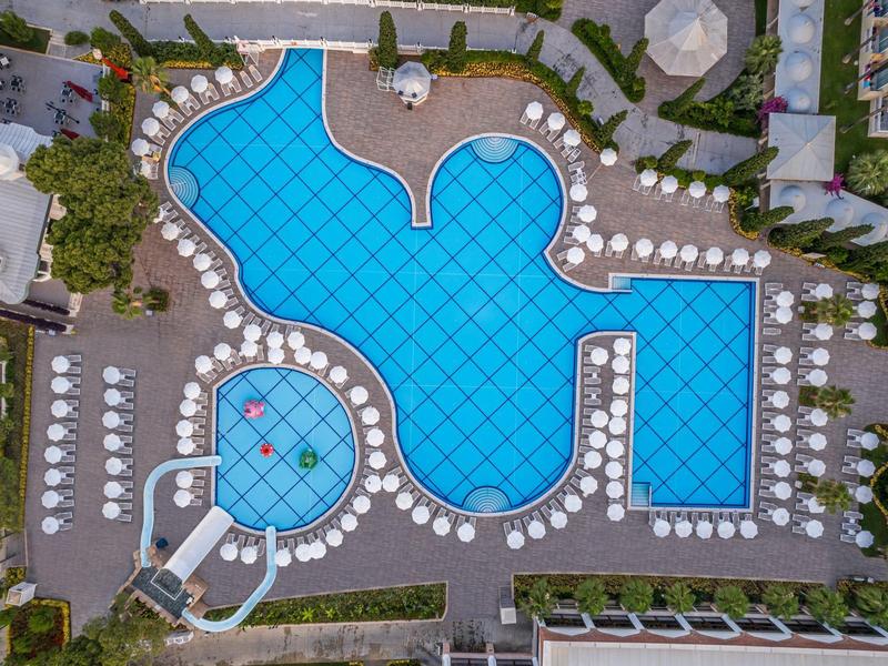 Luchtfoto van een groot hotelzwembad met ligstoelen en parasols omringd door verzorgde tuinen.