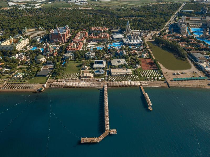Luchtfoto van een kustresort met een lange pier in zee en verschillende gebouwen en zwembaden.
