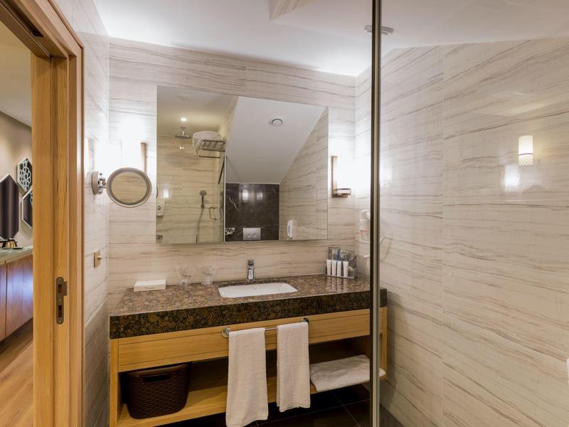 Modern hotelbadkamer met wastafel, spiegel, handdoeken en inloopdouche met glazen wand.