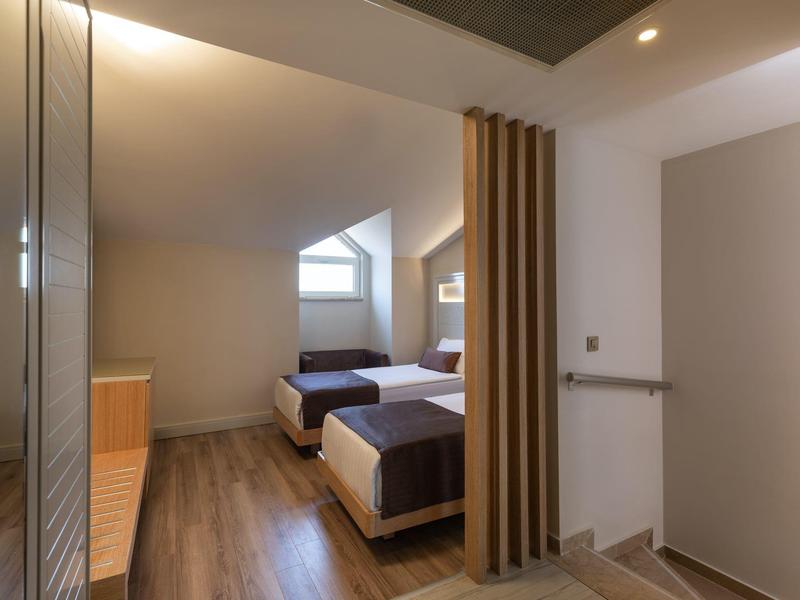 Eenvoudige hotelkamer met twee eenpersoonsbedden, houten vloer en schuin dakraam.