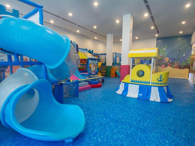 Kleurrijke overdekte speeltuin met blauwe glijbaan en speelstructuren op blauwe vloer.