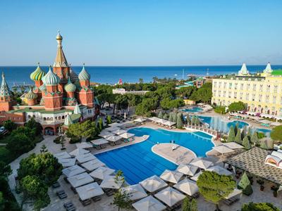Großer Hotelpool mit Liegestühlen neben einer bunten Kirche und Meer im Hintergrund