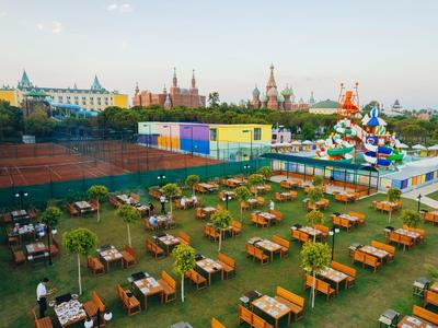 Großer Außenbereich mit vielen Holztischen und buntem Karussell im Hinterhof vor historischen Gebäuden.