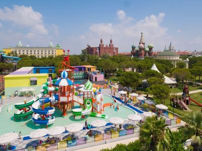 Bunte Wasserspielplatzanlage neben einem Hotel mit bunten Gebäuden und Kirchen im Hintergrund.