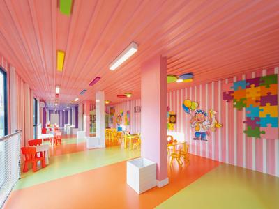 Bunter Kinderspielraum mit rosa Wänden, buntem Deckenlicht und kleinen Tischen im Hotel.