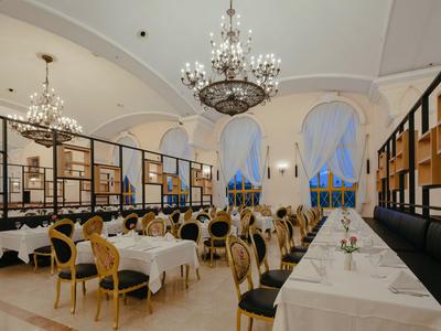 Elegantní restaurace s vysokými stropy, lustry a klasickým dřevěným nábytkem.