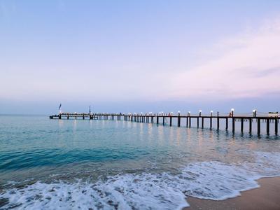 Langer Steg erstreckt sich ins ruhige blaue Meer bei klarem Himmel mit sanften Wellen am Sandstrand.