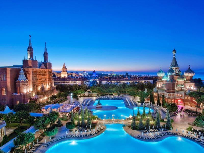 Nächtliche Stadtansicht mit beleuchtetem Schwimmbad und historischen Gebäuden unter klarem Himmel.