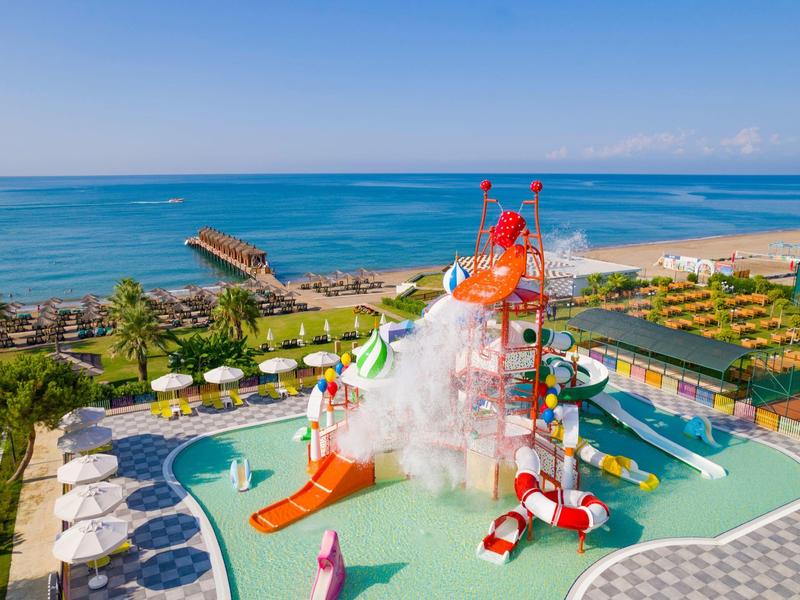 Wasserpark mit farbenfrohen Wasserrutschen und Planschbecken am Strand mit Blick auf das Meer.