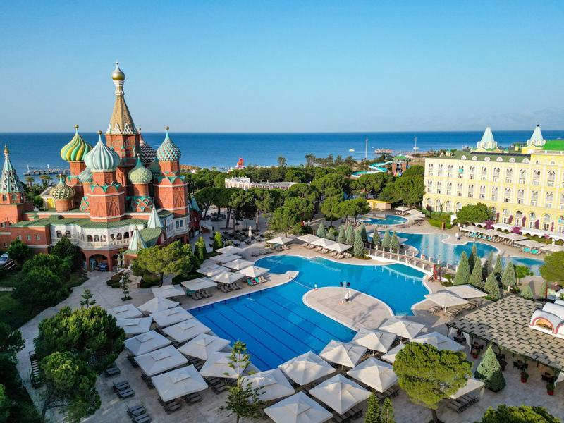 Großer Hotelpool mit Liegestühlen neben einer bunten Kirche und Meer im Hintergrund