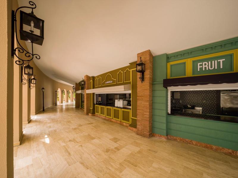 Ein leerer Flur mit einem Stand für Obst und einem Informationsfenster in einem Hotel.