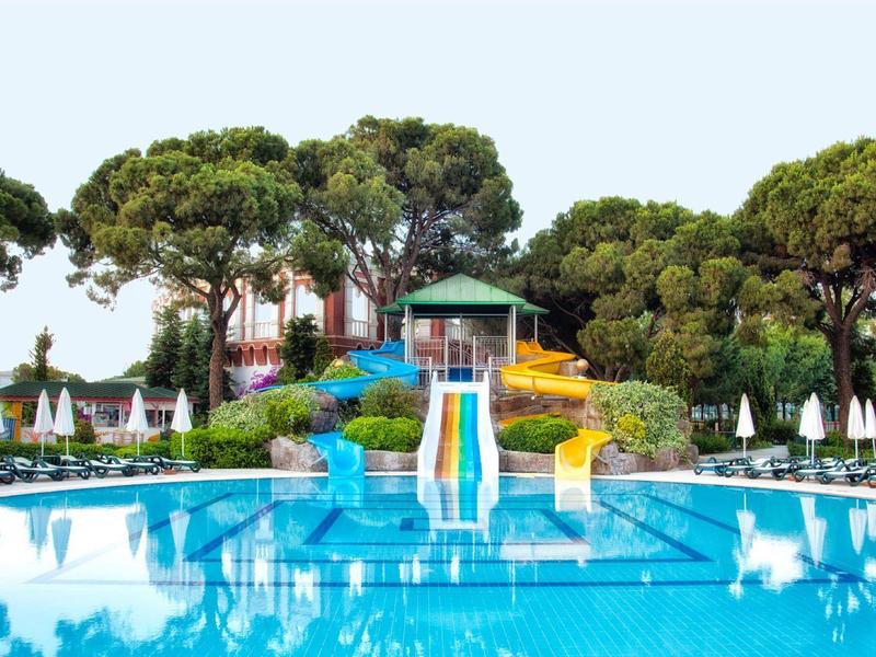 Aquapark mit großem blauen Pool, Rutschen und grünen Bäumen im Hintergrund.