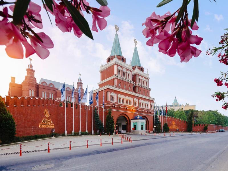 Rotes Backsteingebäude mit Tor, Türmen und Zinnen vor blauem Himmel, umrahmt von pinken Blüten.