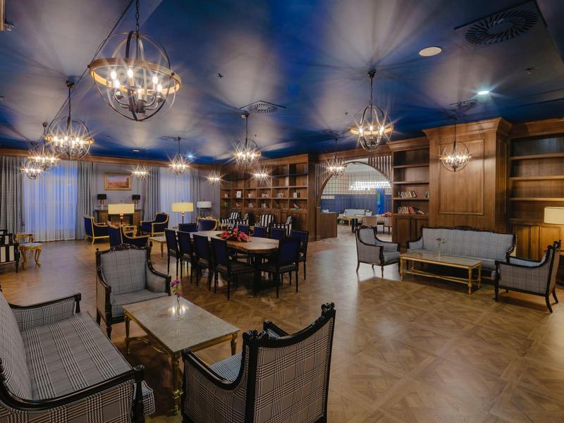 Eleganter Gastraum mit Holzregalen, blauen Decken, gemütlichen Sofas und edlen Kronleuchtern.