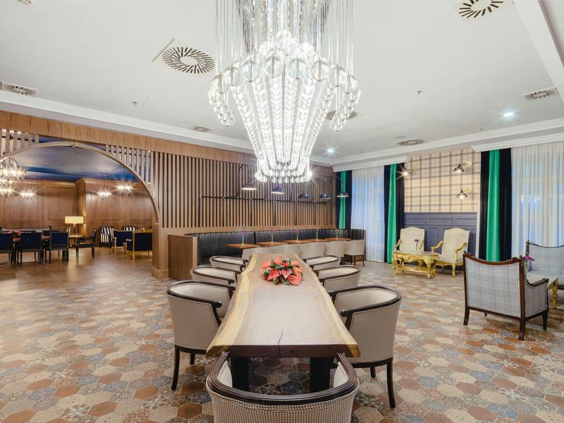 Eleganter Speiseraum mit langem Holztisch, bequemen Sesseln und großer Kristall-Deckenleuchte.