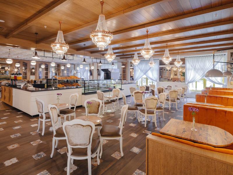 Großer, heller Saal mit weißen Stühlen, Holzbalkendecke und modernen Kronleuchtern.