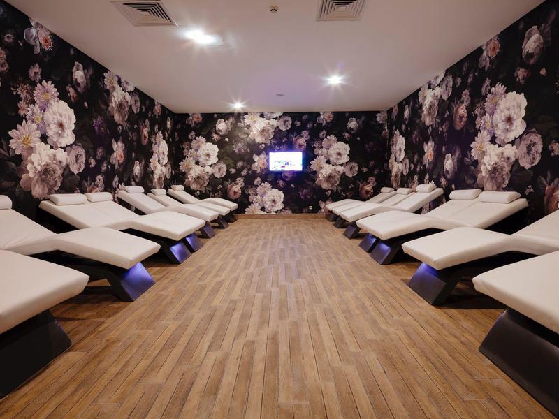 Entspannungsraum mit weißen Liegen, Holzfußboden und dunkler Wand mit großen Blumenmuster.